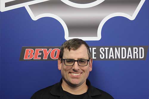 Smiling person in front of 'Beyond the Standard' sign.